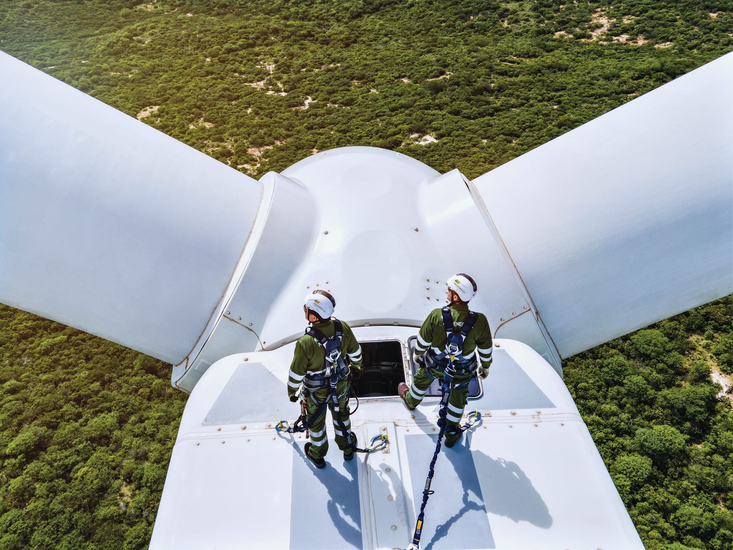 Two technicians in safety gear on top of a wind turbine nacelle